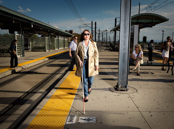 An image of CEO and Founder Claudia Folska walking with her cane alongside railway tracks.